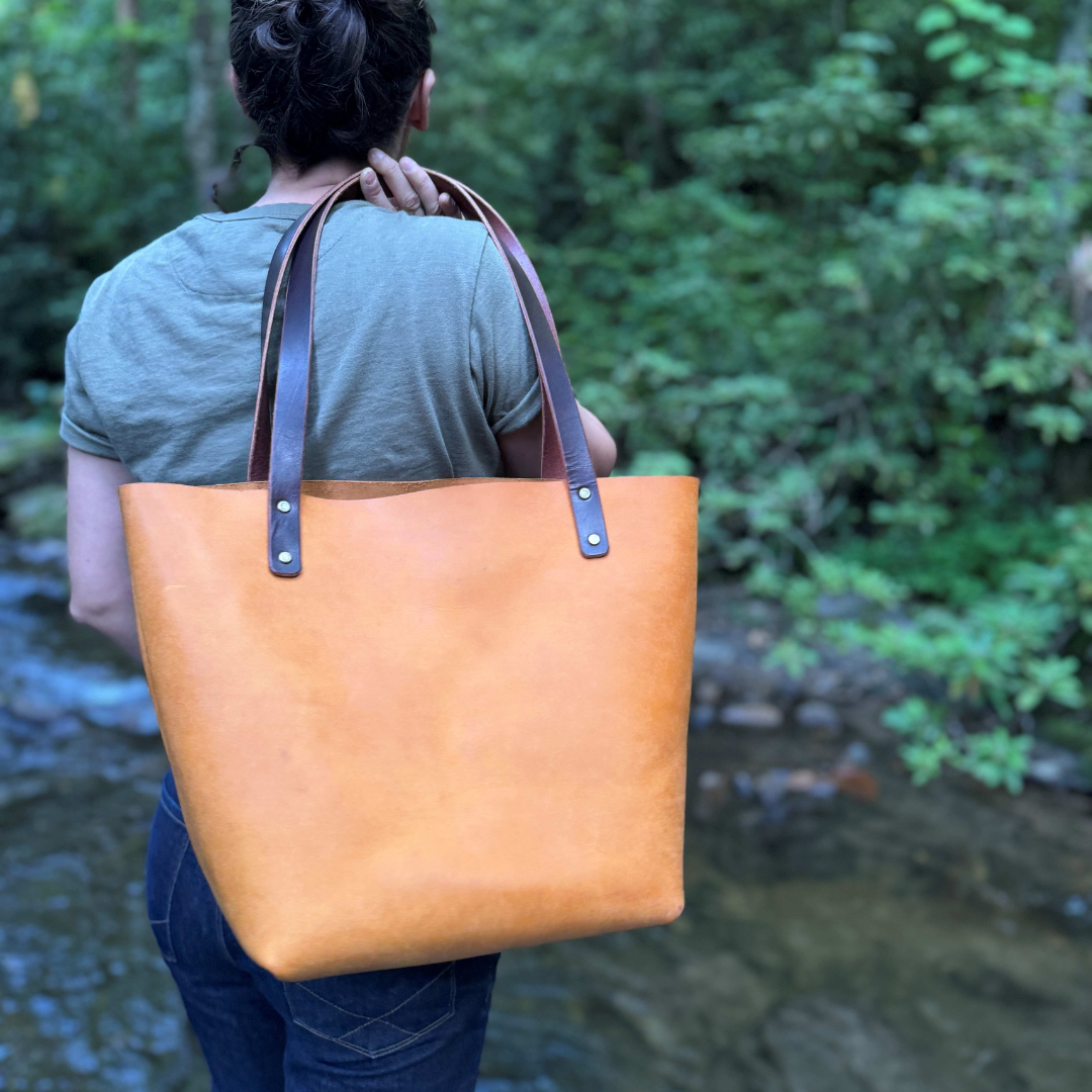 A women holding a yellow leather tote standing by a river.