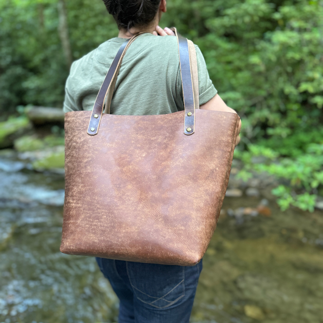 A women holding a brown leather tote standing by a river.