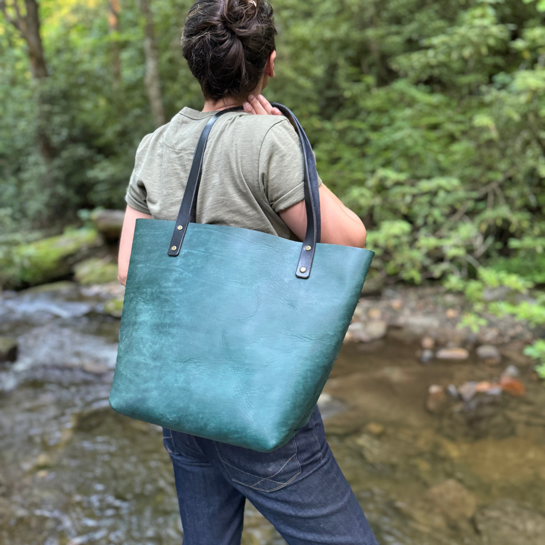 A women holding a turquoise leather tote bag standing by a river.