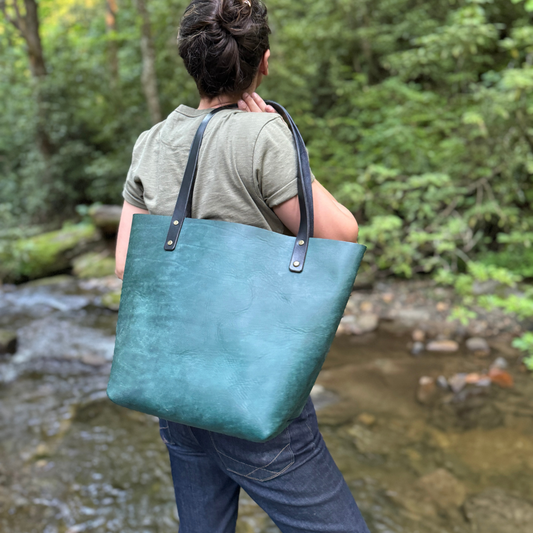 A women holding a turquoise leather tote bag standing by a river.