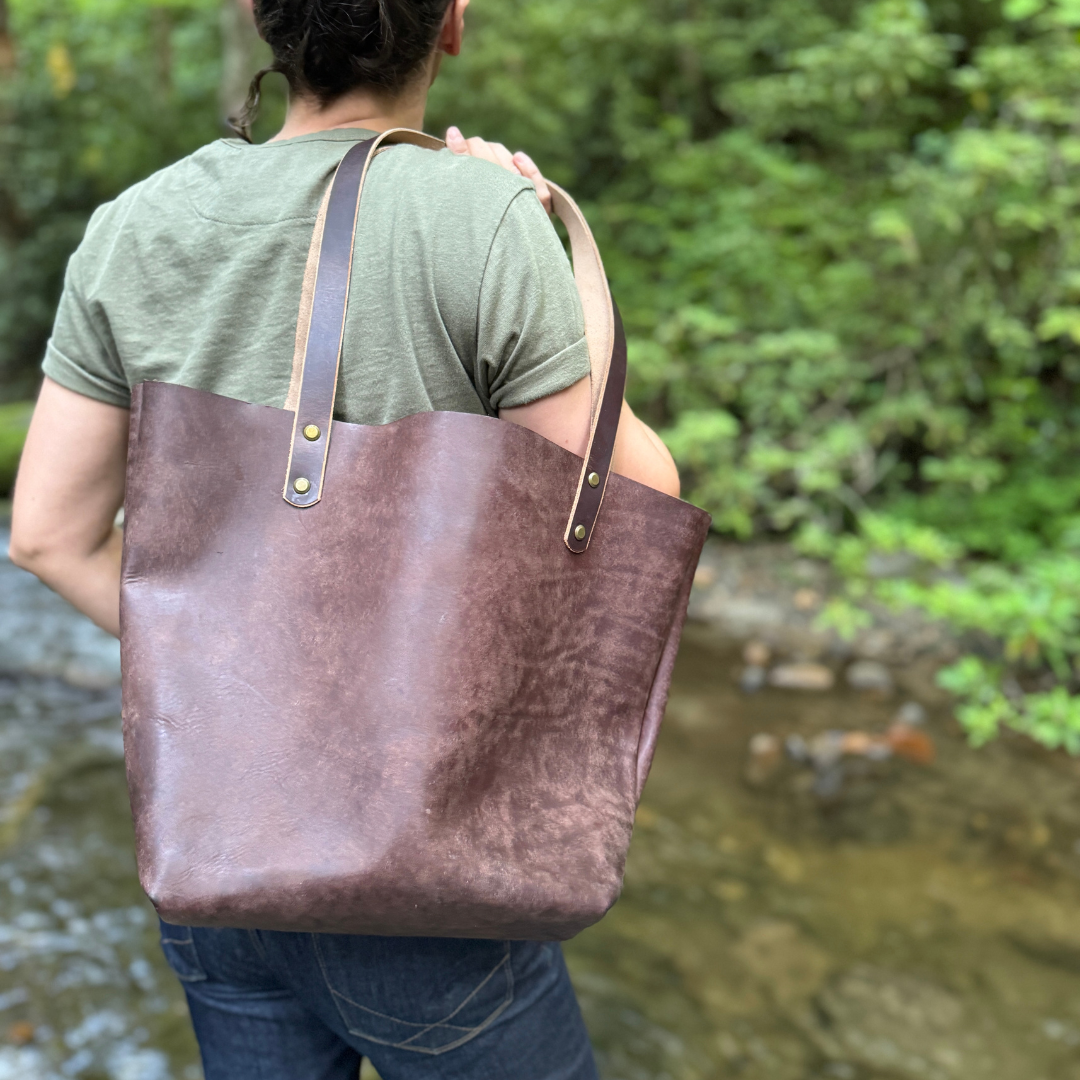 A women holding a brown leather tote standing by a river.