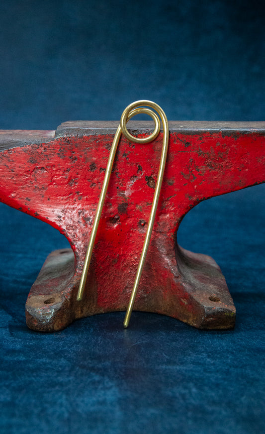 A brass hairpin resting on a red anvil.
