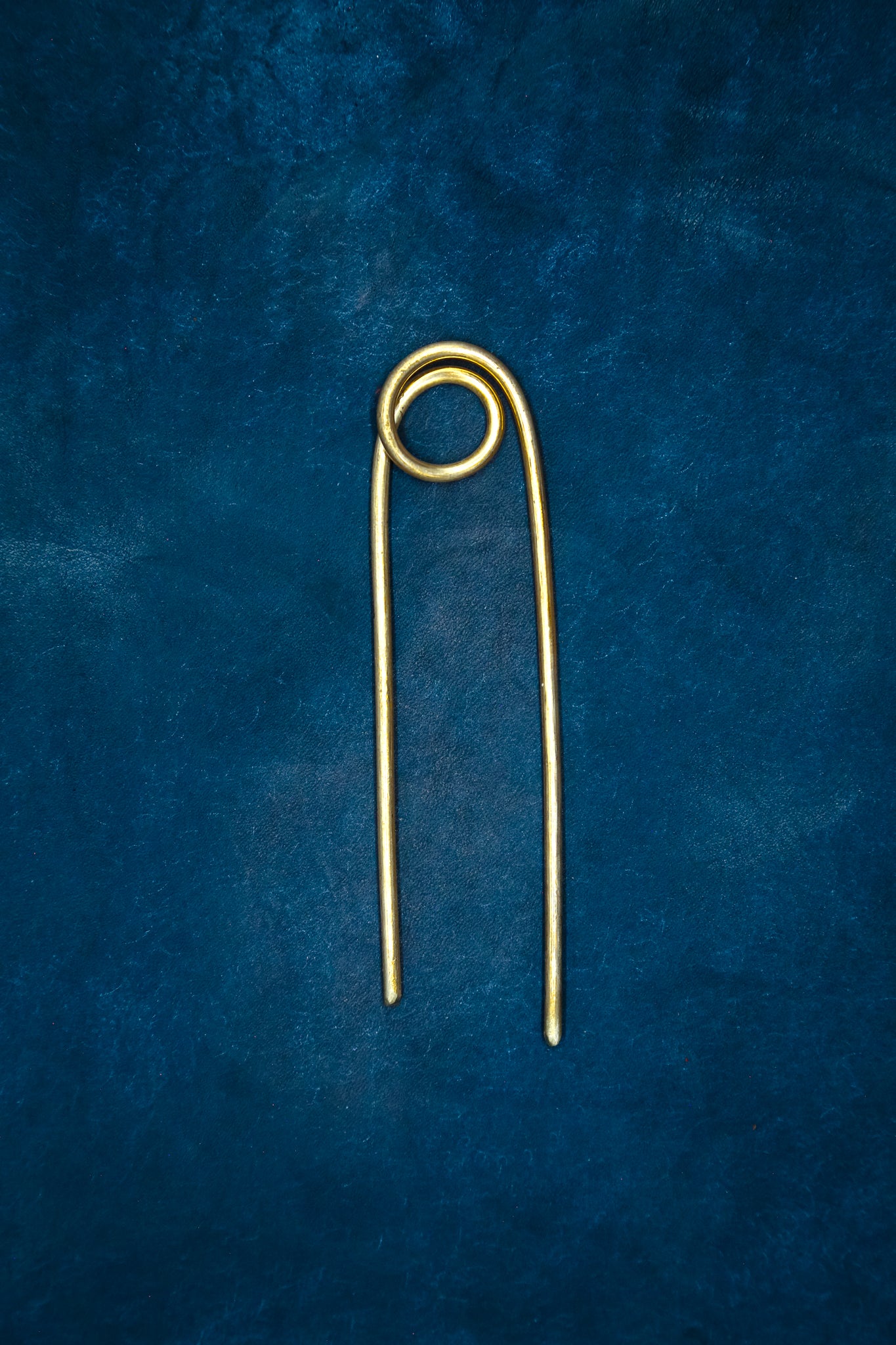 A brass hairpin on blue leather.