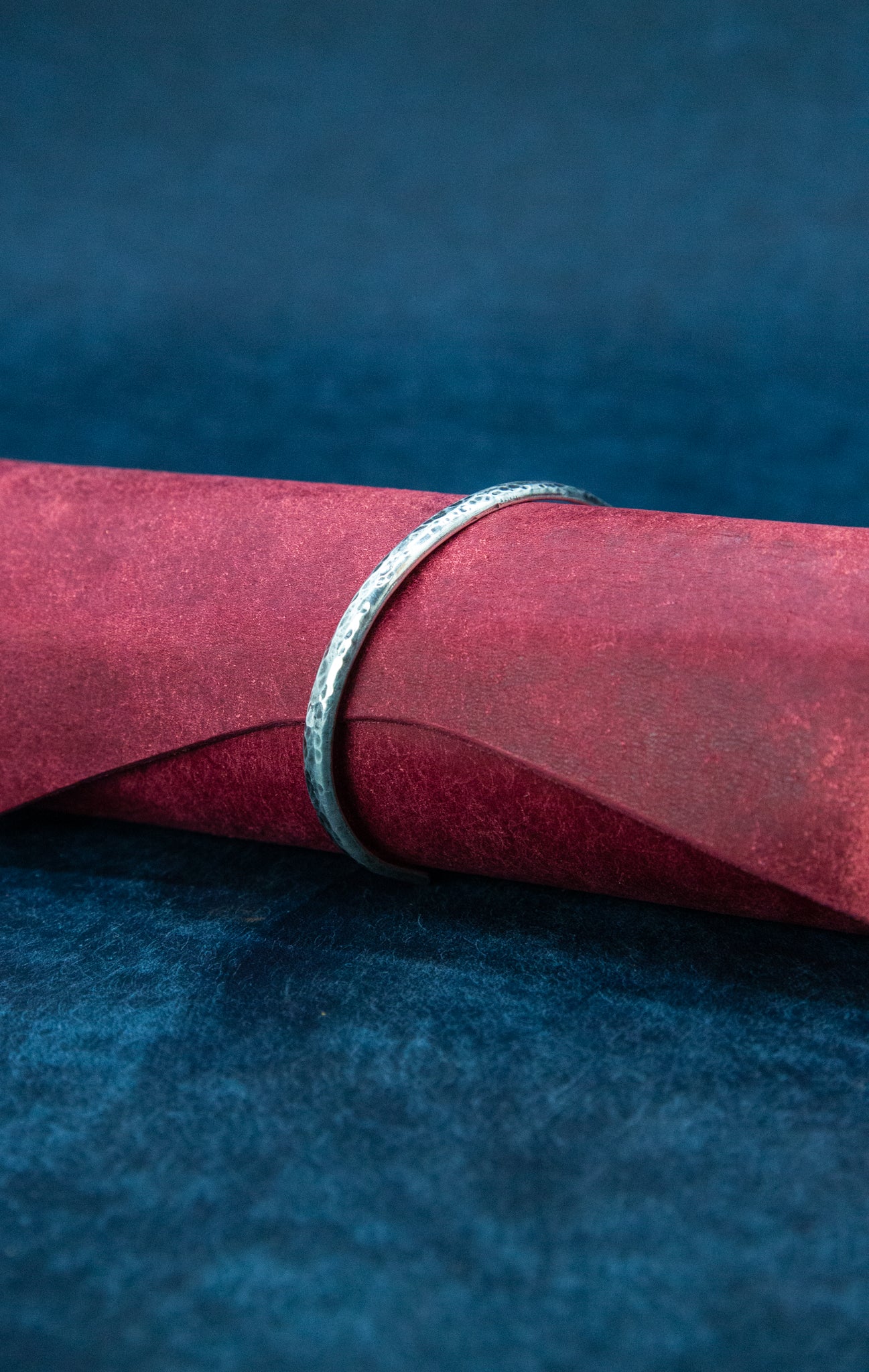A silver oxidized cuff bracelet on a roll of red leather.