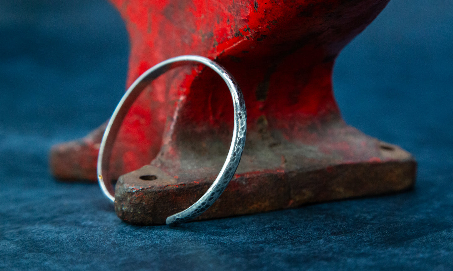 A silver oxidized cuff bracelet resting on a red anvil