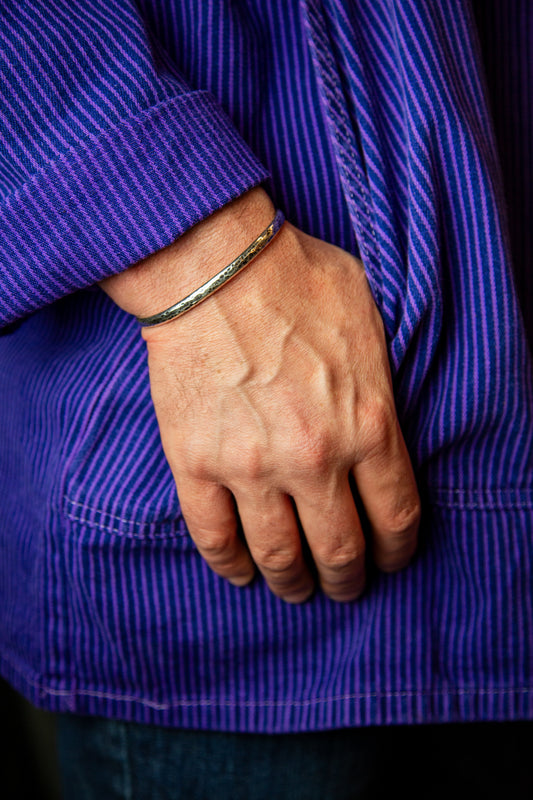 A hand resting in the pocket of a purple striped jacket wearing a silver oxidized cuff bracelet.