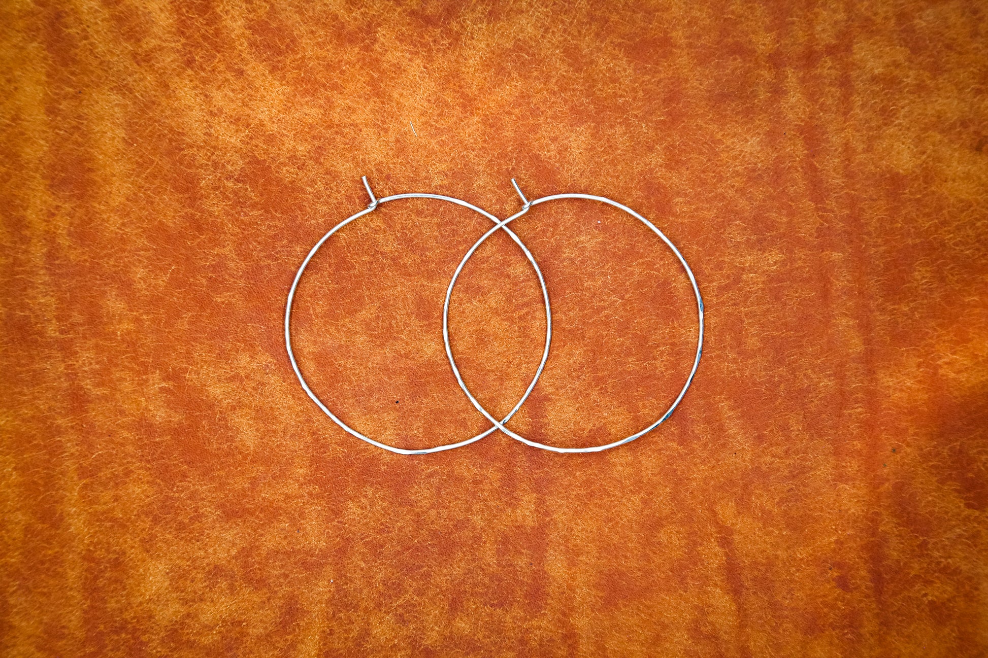 Two sterling silver hoops on burnt orange leather.