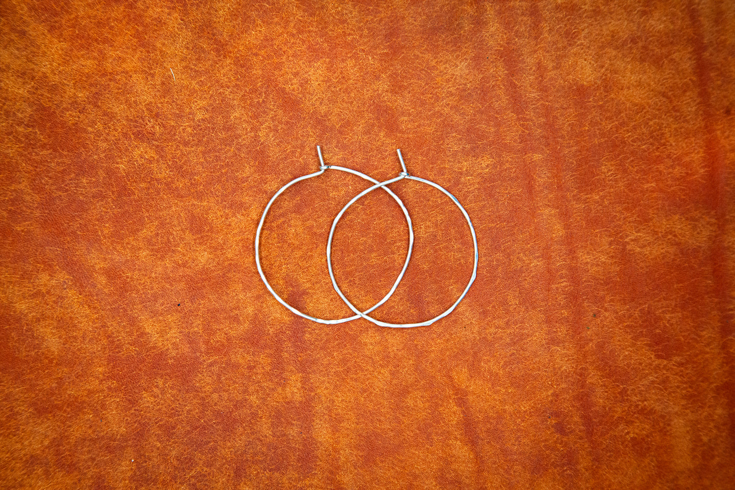 Two sterling silver hoops on burnt orange leather.