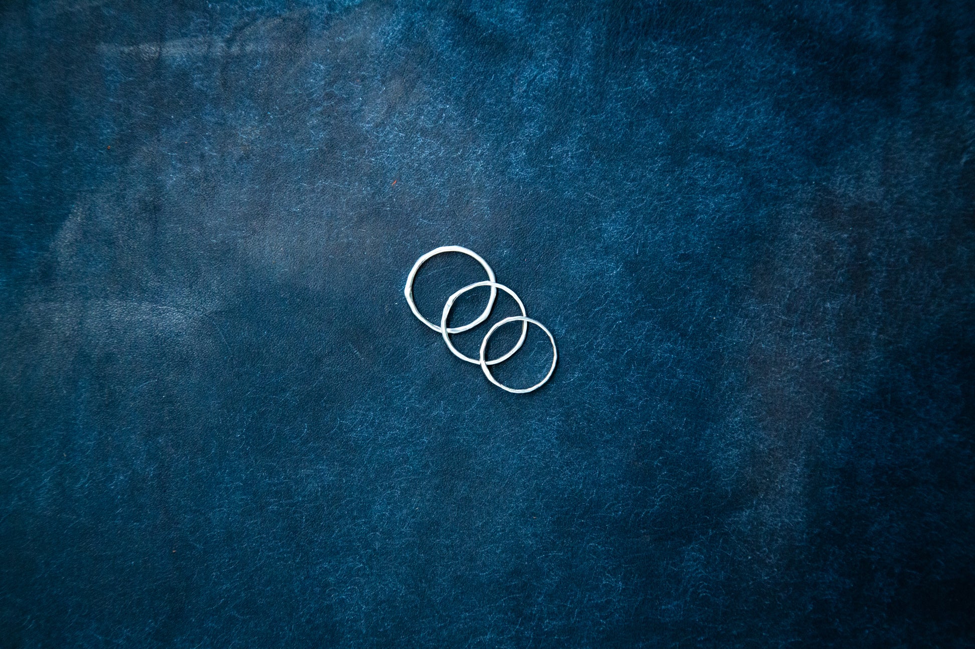 Three silver rings on blue leather.