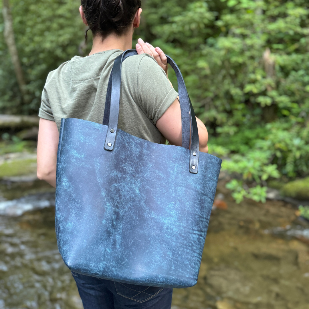 A women holding a blue leather tote standing by a river.