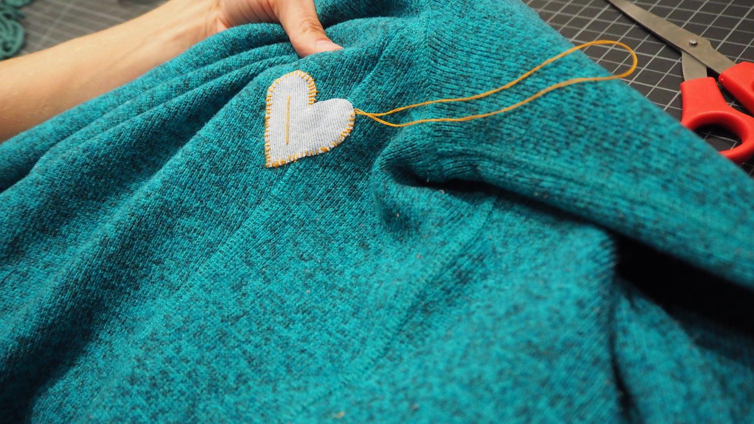 A closeup of someone stitching a heart patch onto a jacket.